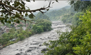 নেপালত পুনৰ প্ৰকৃতিৰ তাণ্ডৱ! বুঢ়ী গণ্ডকী নদীৰ প্ৰলয়ংকাৰী বানত উটিল ৬খন দলং আৰু ৩৫টা বাসগৃহ, সন্ধানহীন ১০ জন লোক A swollen river flowing through a green hillside settlement, supplied with the Nepal flood report